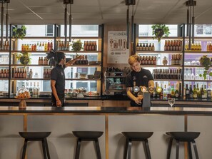 Zona de bar con estantes llenos de botellas y vasos, un cartel con la carta y taburetes.