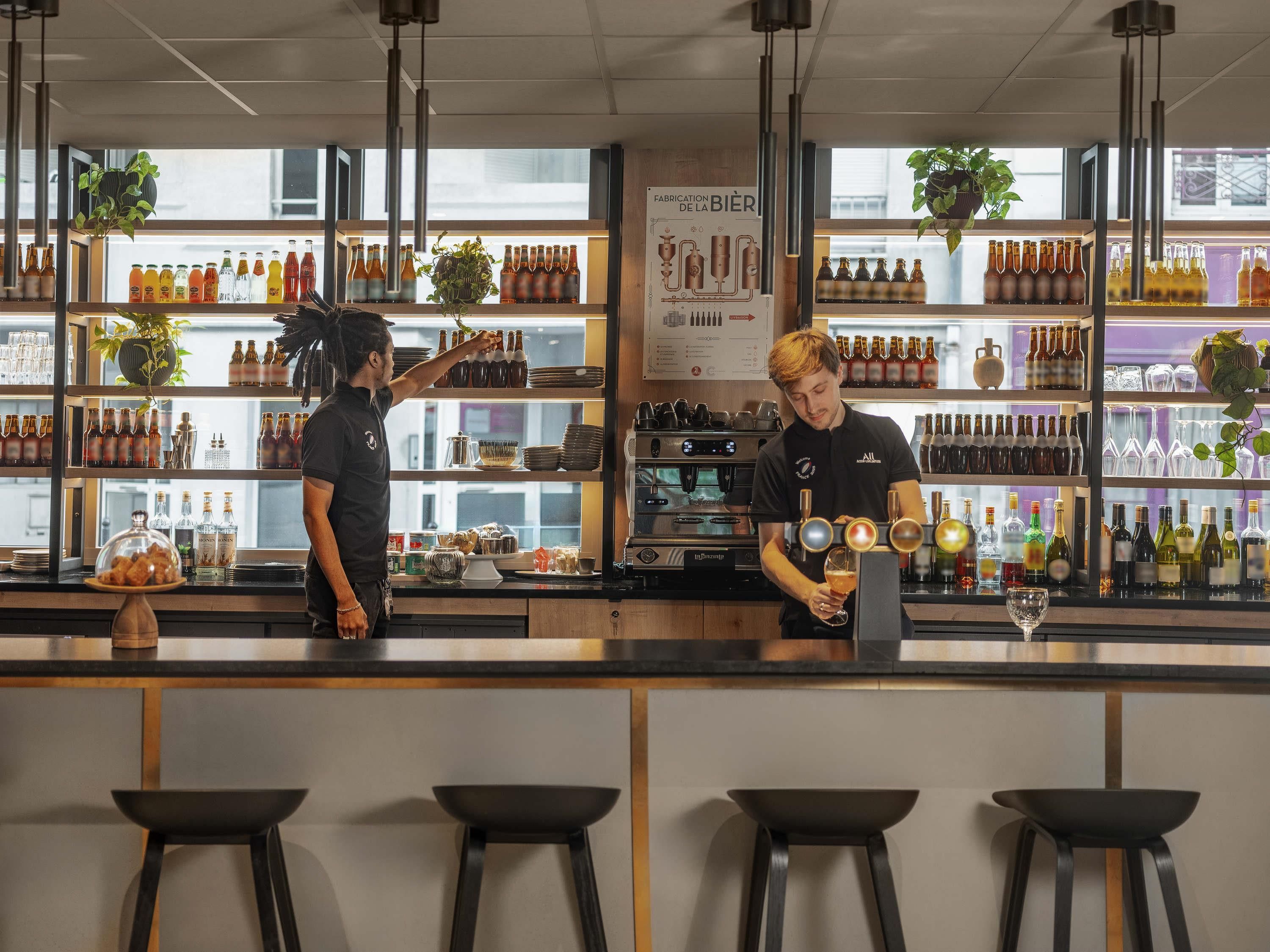 A bar area with shelves of bottles and glasses, a menu board, and stools.