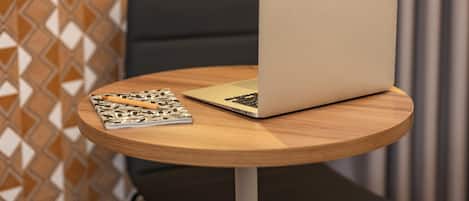 A laptop on a round wooden table with a notebook and pen beside it.