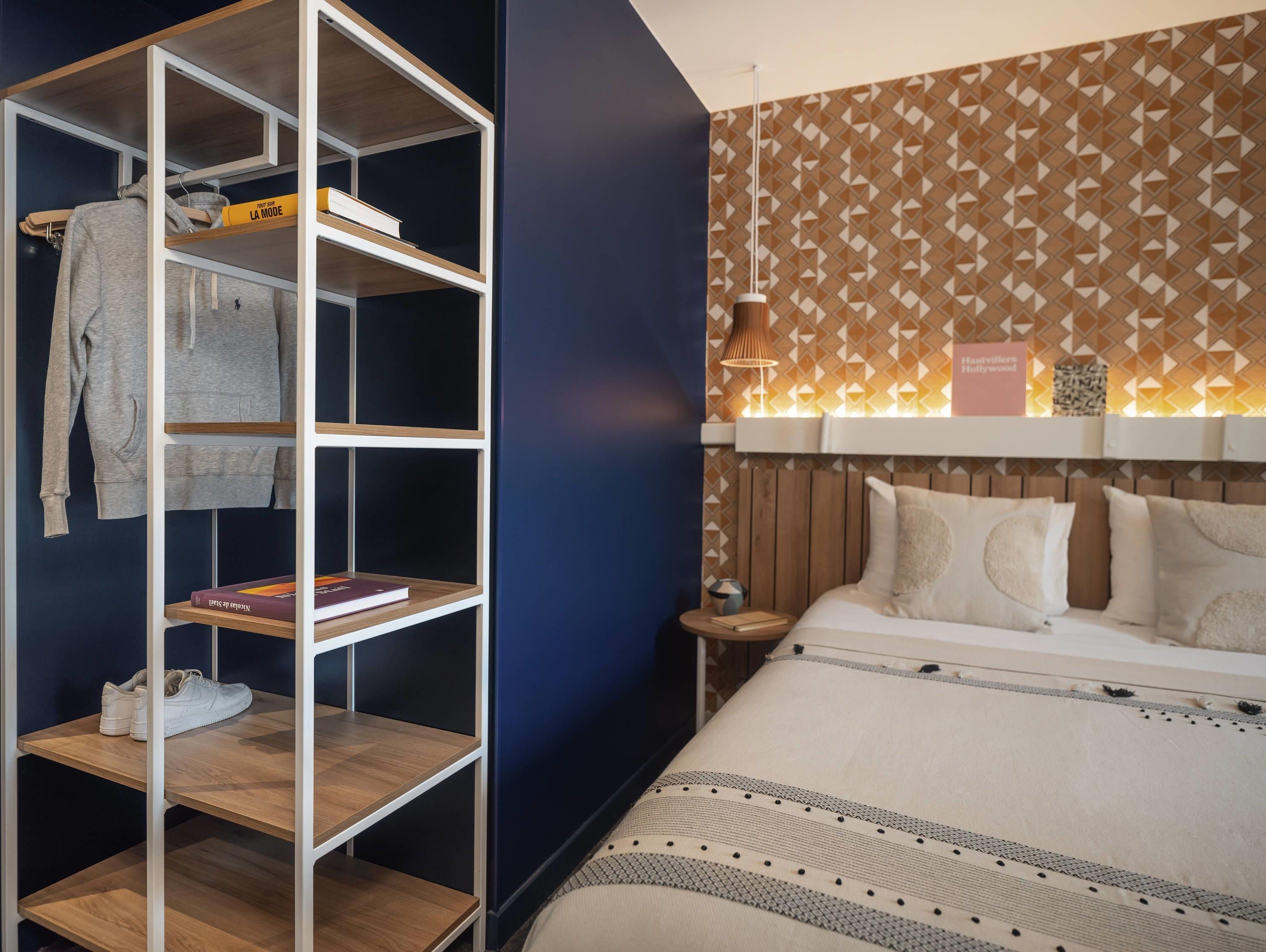 Un dormitorio con una cama, un armario con estantes y una pared con estampado.