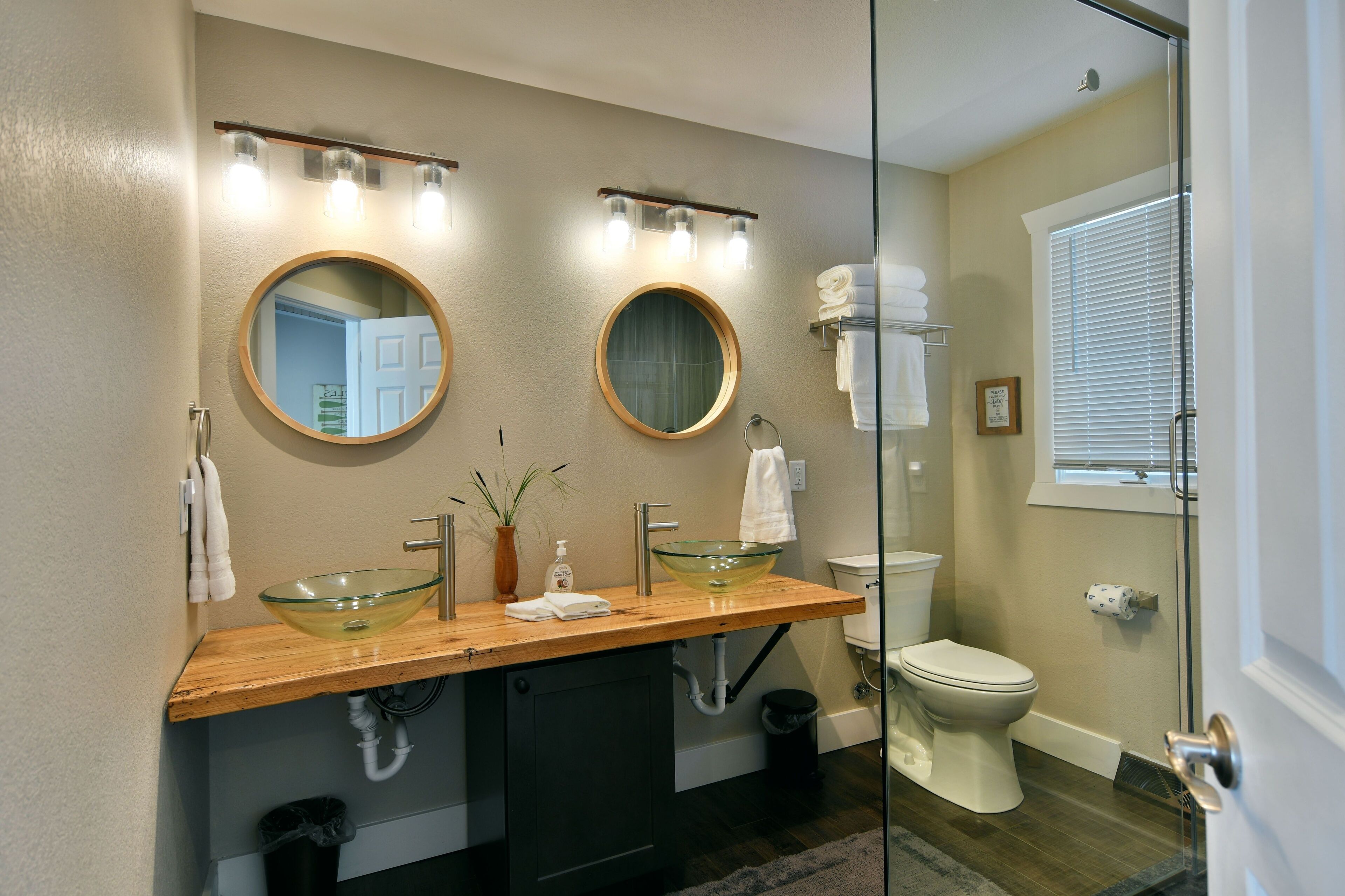 A bathroom with two sinks, a glass bowl sink, a mirror, and a shower.