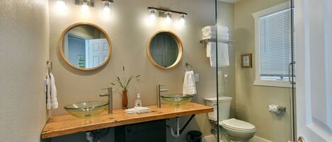 A bathroom with two sinks, a glass bowl sink, a mirror, and a shower.