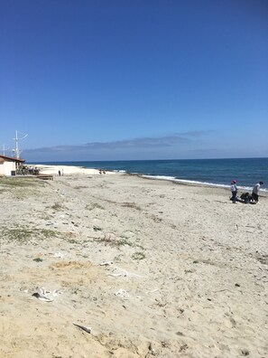 Ein Strand mit einem Gebäude links, blauem Himmel und dem Meer im Hintergrund.