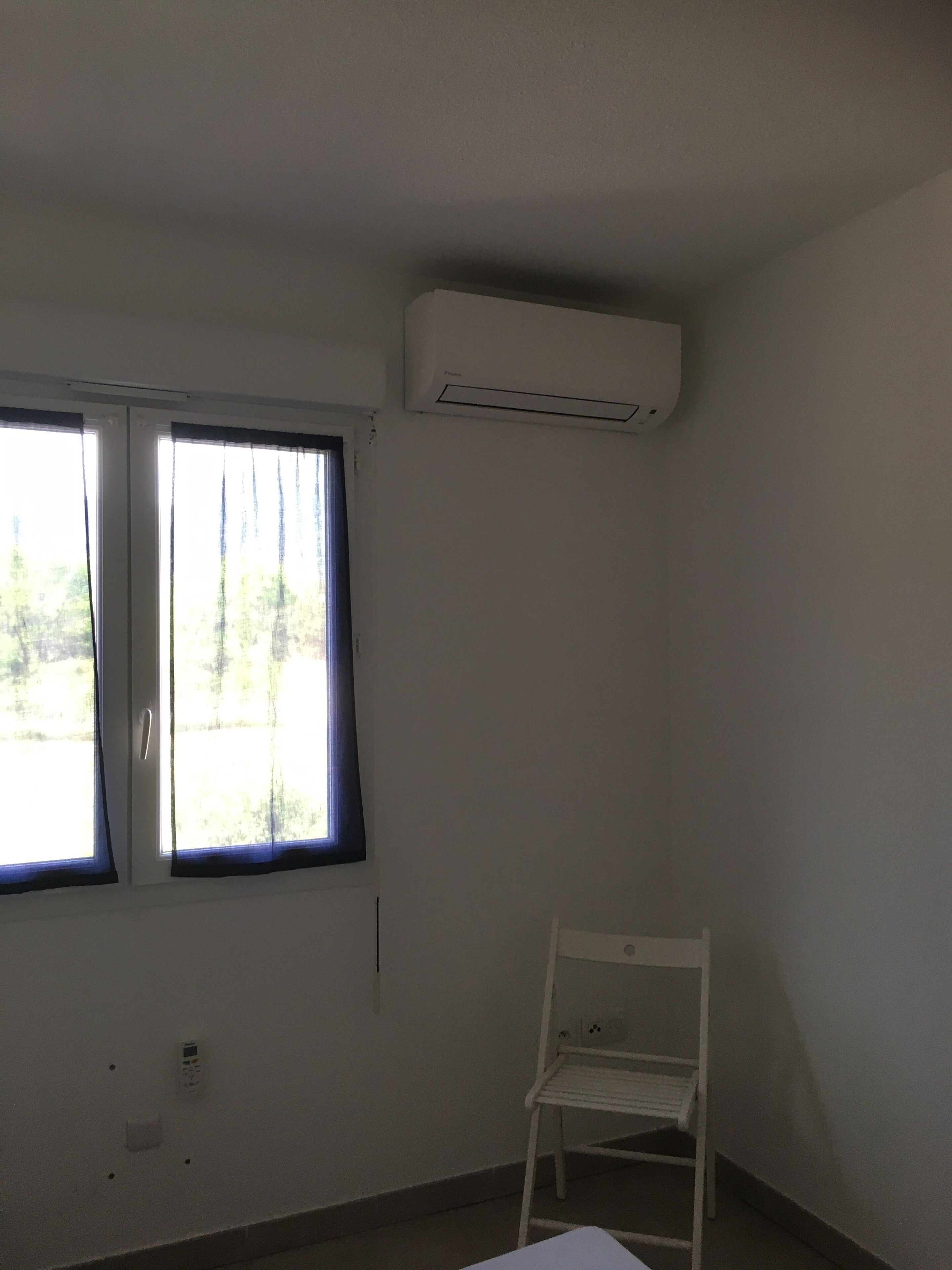 Une pièce avec une fenêtre, un climatiseur et une chaise blanche.