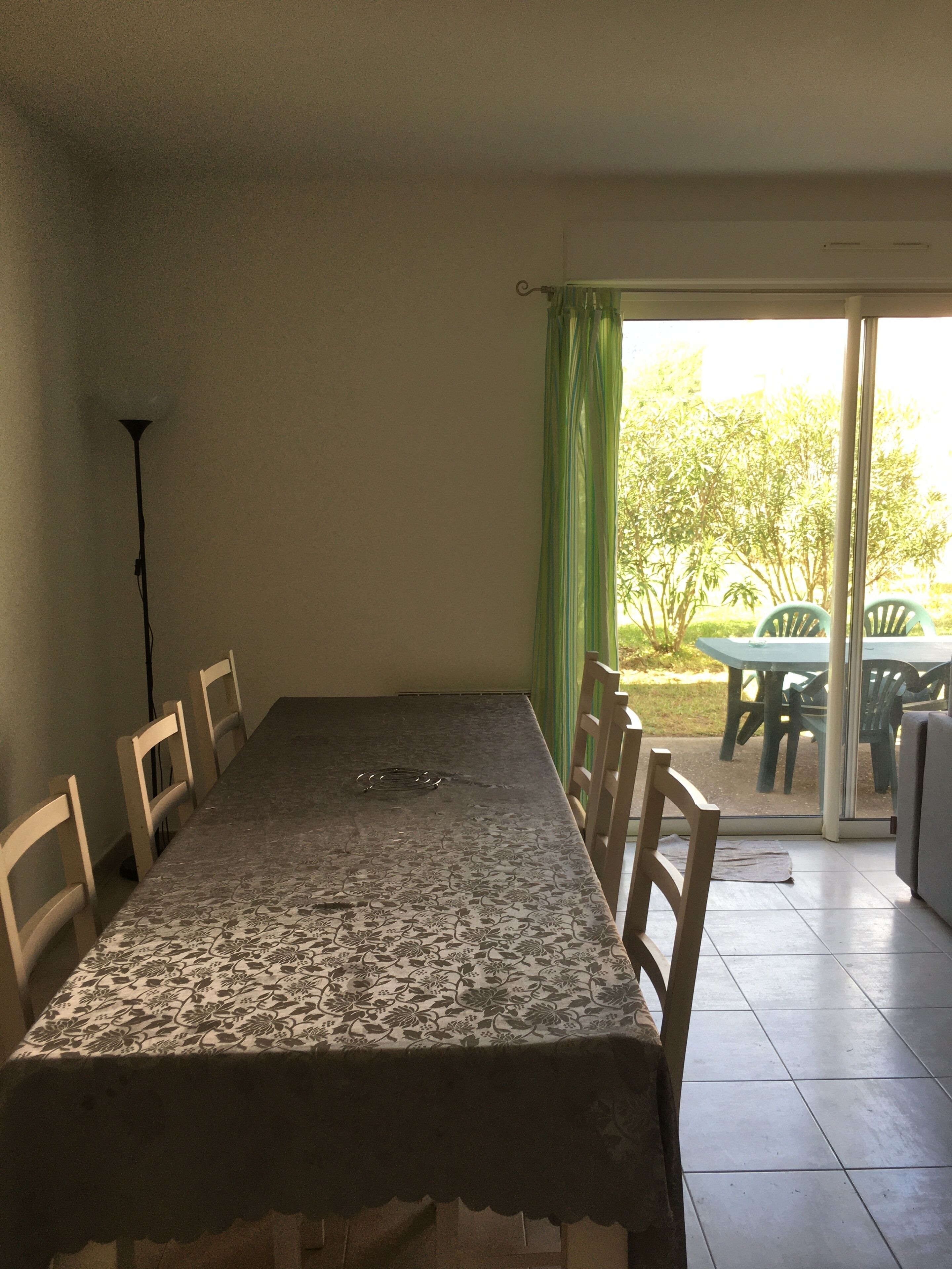 Een eetgedeelte met een tafel en stoelen, een vloerlamp, en uitzicht op een terras met stoelen en een tafel.