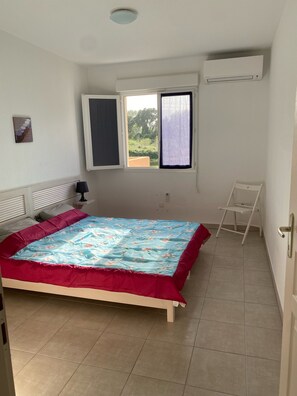 Una camera da letto con un letto, una finestra, un condizionatore d'aria e un tavolino.