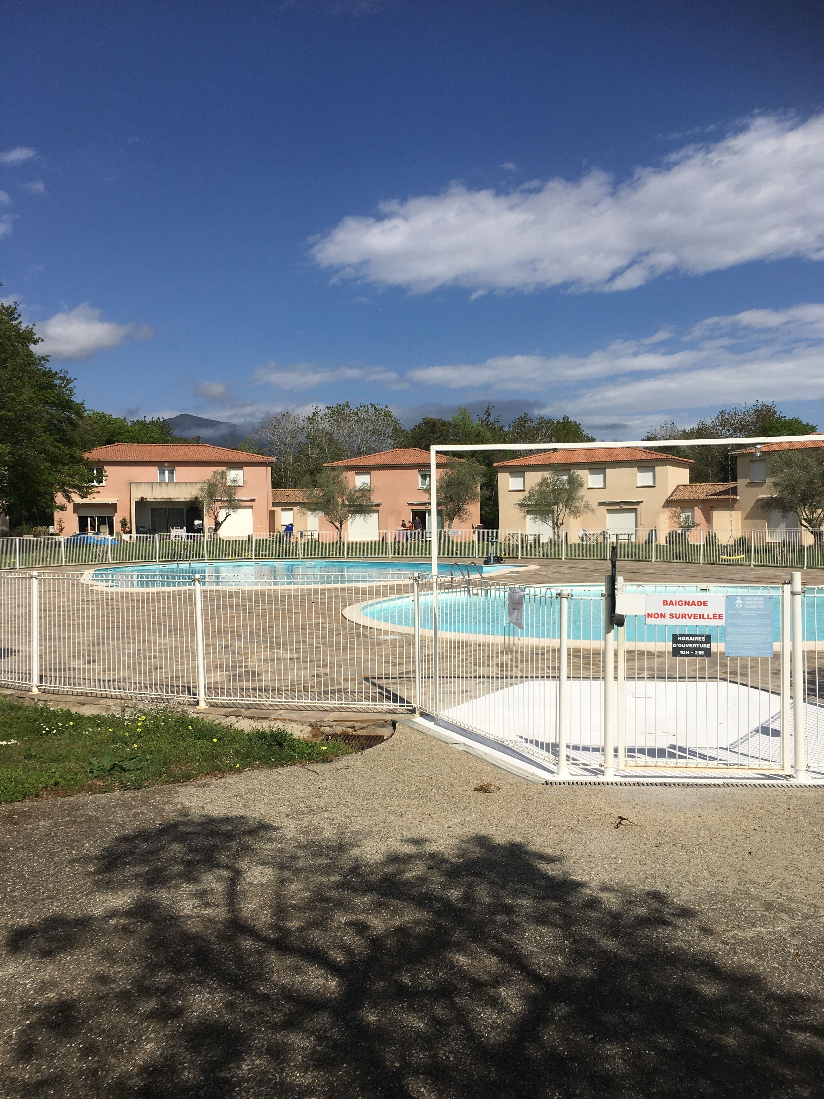 Zona residencial con piscina, rodeada por una cerca blanca y edificios con fachada rojiza.
