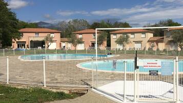 Zona residencial con piscina, rodeada por una cerca blanca y edificios con fachada rojiza.