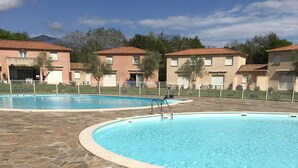 Piscina com pavimento de pedra, rodeada por edifícios com telhados em tijolo vermelho.