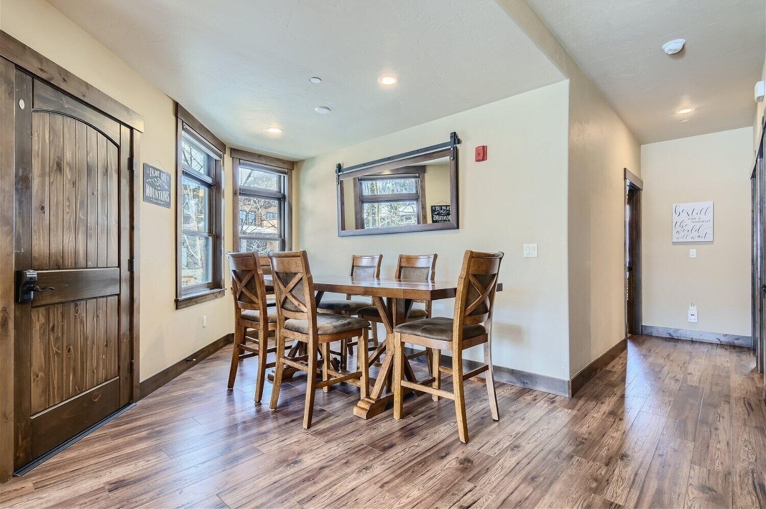 A dining area with a wooden table and chairs, large windows, and a wooden door.