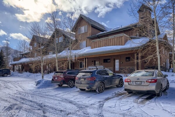 A building with a wooden facade and multiple windows, parked cars in front, and snow on the ground.