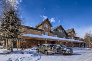 A large lodge with multiple buildings, a snow-covered driveway, and a parked SUV.
