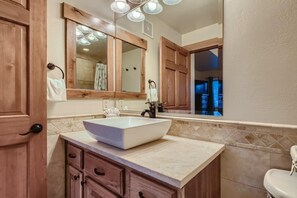 A bathroom with a large vessel sink, wooden cabinets, a mirror, and a window.