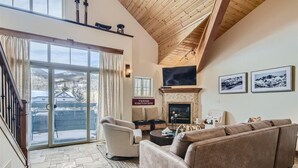 Un salón espacioso con chimenea, asientos cómodos y un ventanal con vistas a un paisaje nevado.