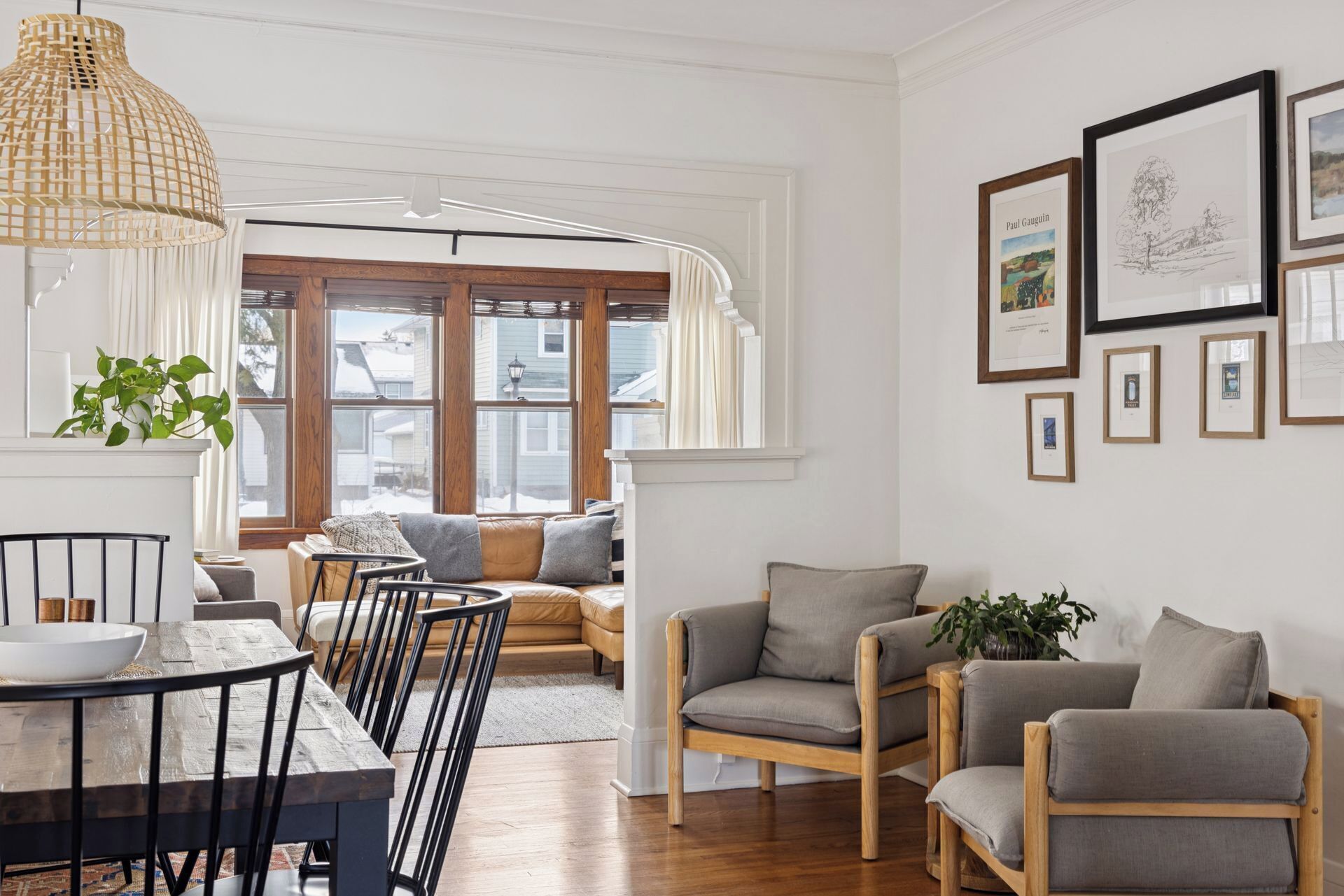 Ein gemütliches Wohnzimmer mit einem Holzesstisch, Stühlen, einer Couch und einem großen Fenster mit Vorhängen.