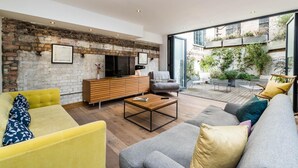 A spacious living area with a brick wall, a large TV, and a cozy seating arrangement including a yellow sofa and a grey couch.