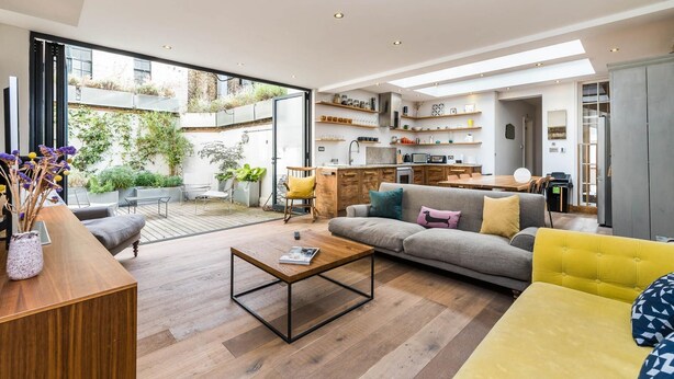 A modern living room with a sofa, coffee table, and a dining area with a kitchen in the background.