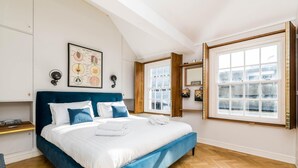 A bedroom with a large bed, a wooden floor, a window with a view, and a wall-mounted light fixture.