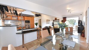 A modern kitchen with stainless steel appliances, a dining area with a glass table, and a living space with a sofa and a painting. - Gorgeous 3BD Cottage in the Heart of Guildford (Guildford)