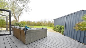 A deck with a wicker sofa and cushions, a metal gate, and a wooden fence. - Gorgeous 3BD Cottage in the Heart of Guildford (Guildford)