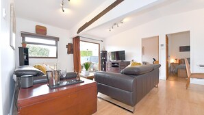 A spacious living room with a grey sofa, wooden coffee table, and a television. There is a wooden cabinet and a plant on the windowsill. - Gorgeous 3BD Cottage in the Heart of Guildford (Guildford)
