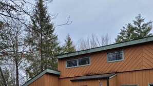 A two-story wooden building with a green garage door, a small porch with steps, and an American flag on the front wall. - Cavalier # 2 3 Bedroom Townhouse by RedAwning (Cable)