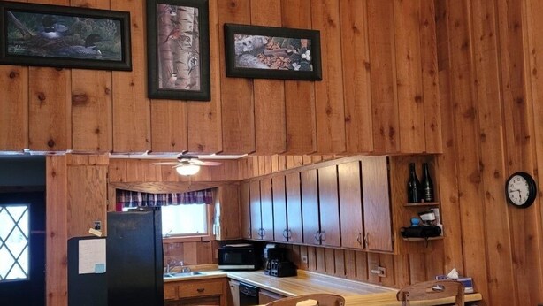 A wooden cabin interior with a kitchen area featuring a bar with stools, a refrigerator, and a microwave. - Cavalier # 2 3 Bedroom Townhouse by RedAwning (Cable)