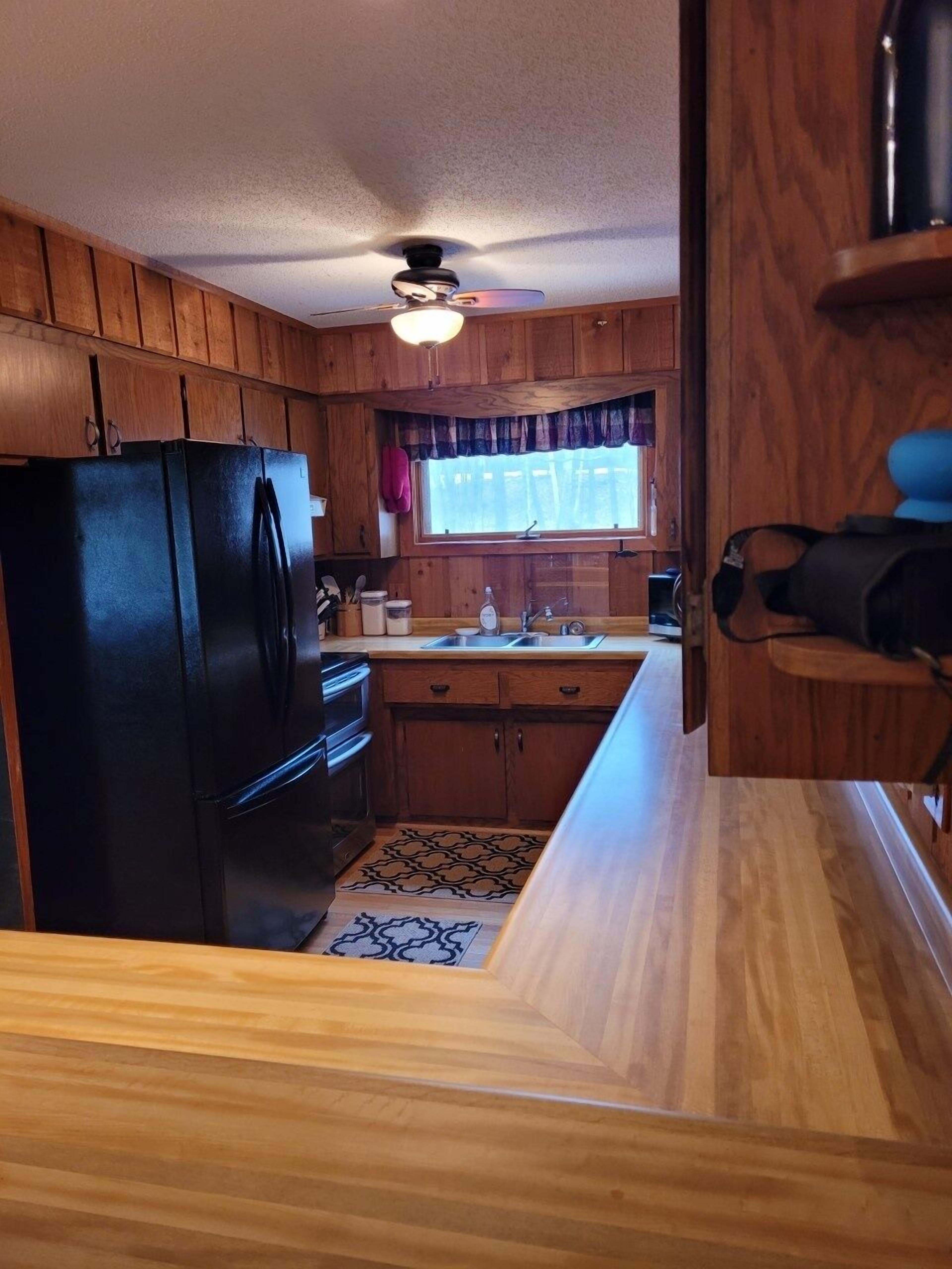 A compact kitchen with wooden cabinets, a black refrigerator, a sink, and a window with a curtain.