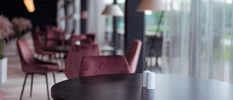 Interior moderno de restaurante con mesas redondas y sillas rojas cómodas, ventanas amplias y lámparas colgantes.