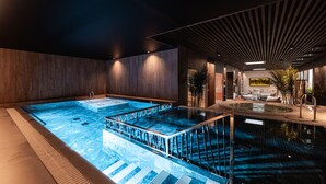 A modern indoor pool area with a central hot tub, surrounded by seating and a wooden wall. - Meri Hotel & SPA (Kuressaare)