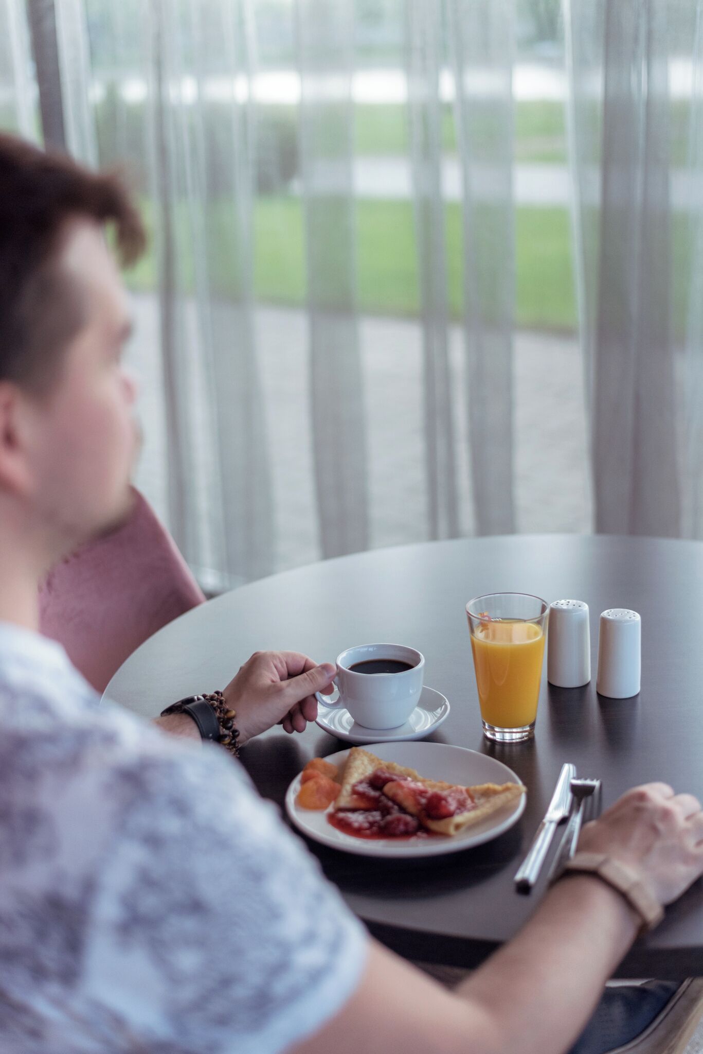 En person sidder ved et rundt bord med en tallerken mad, et glas appelsinjuice og en kop kaffe. Der er salt- og peberkværne på bordet.