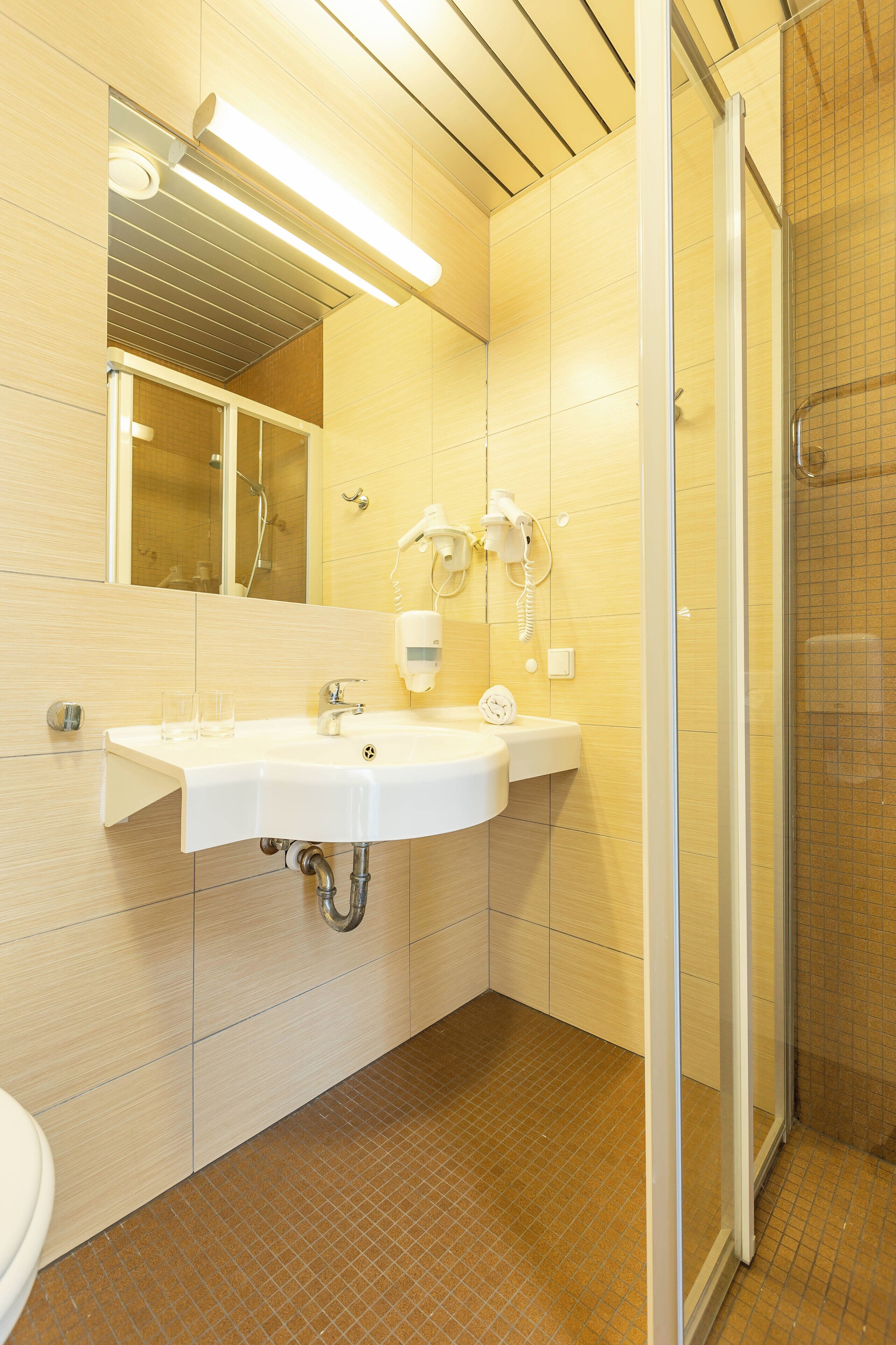 A bathroom with a white sink, a mirror, a shower, and a tiled floor.