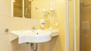 Un baño con lavamanos blanco, espejo, ducha y suelo de baldosas.