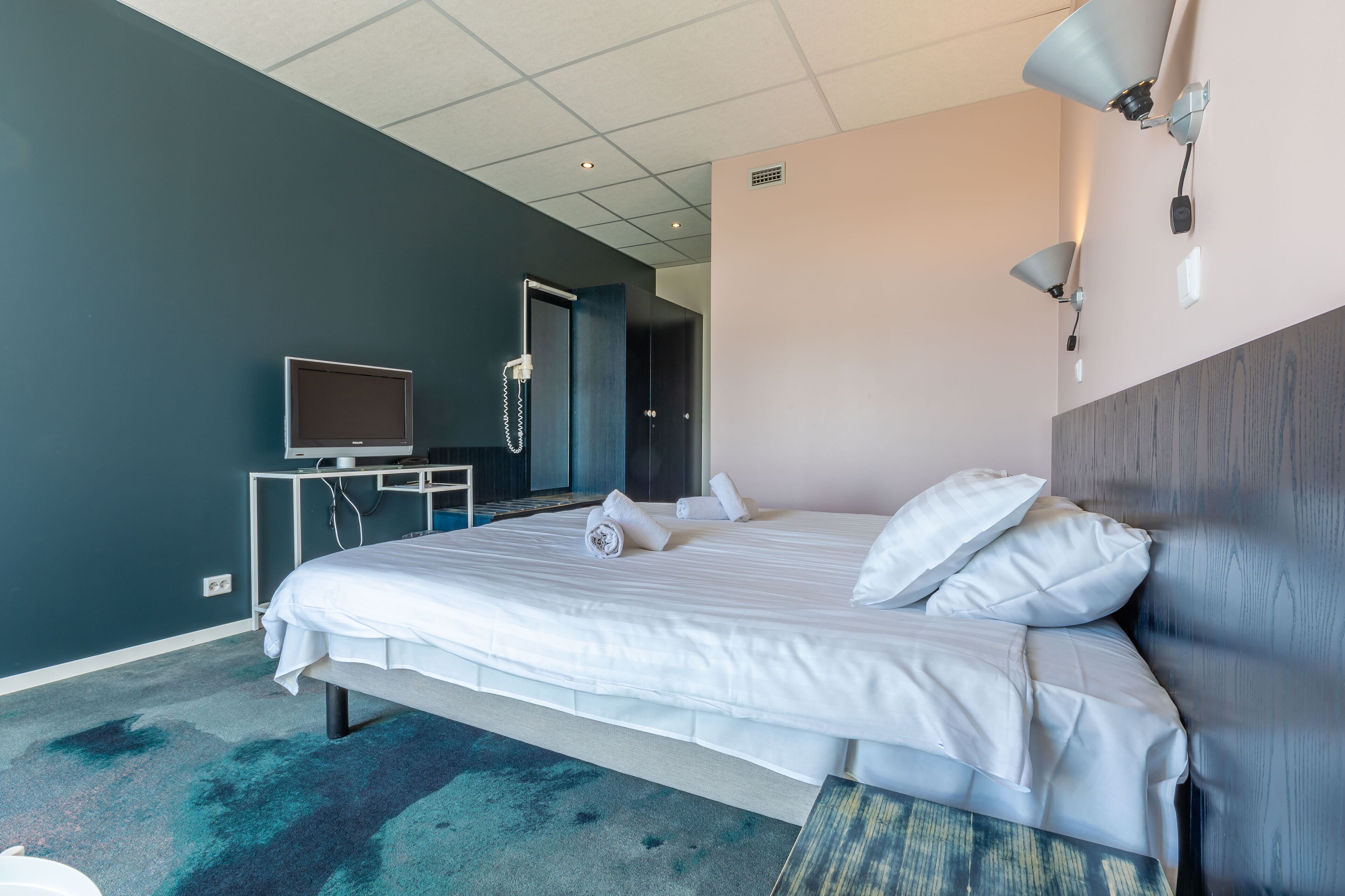 Habitación de hotel con una cama grande, un escritorio con televisor y una puerta que da a otra habitación.