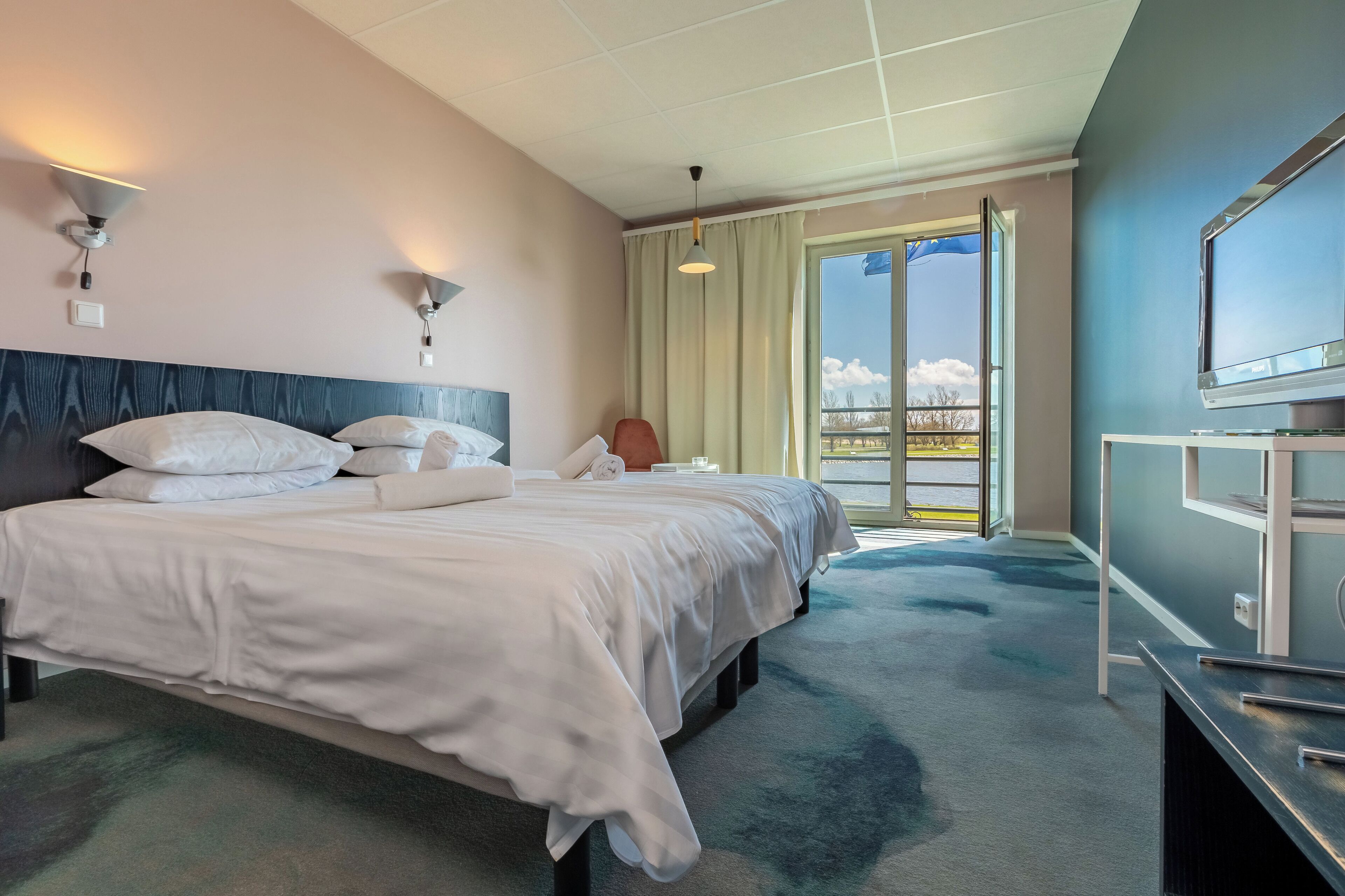 Habitación de hotel con una cama grande, un escritorio, televisión y balcón con vistas.