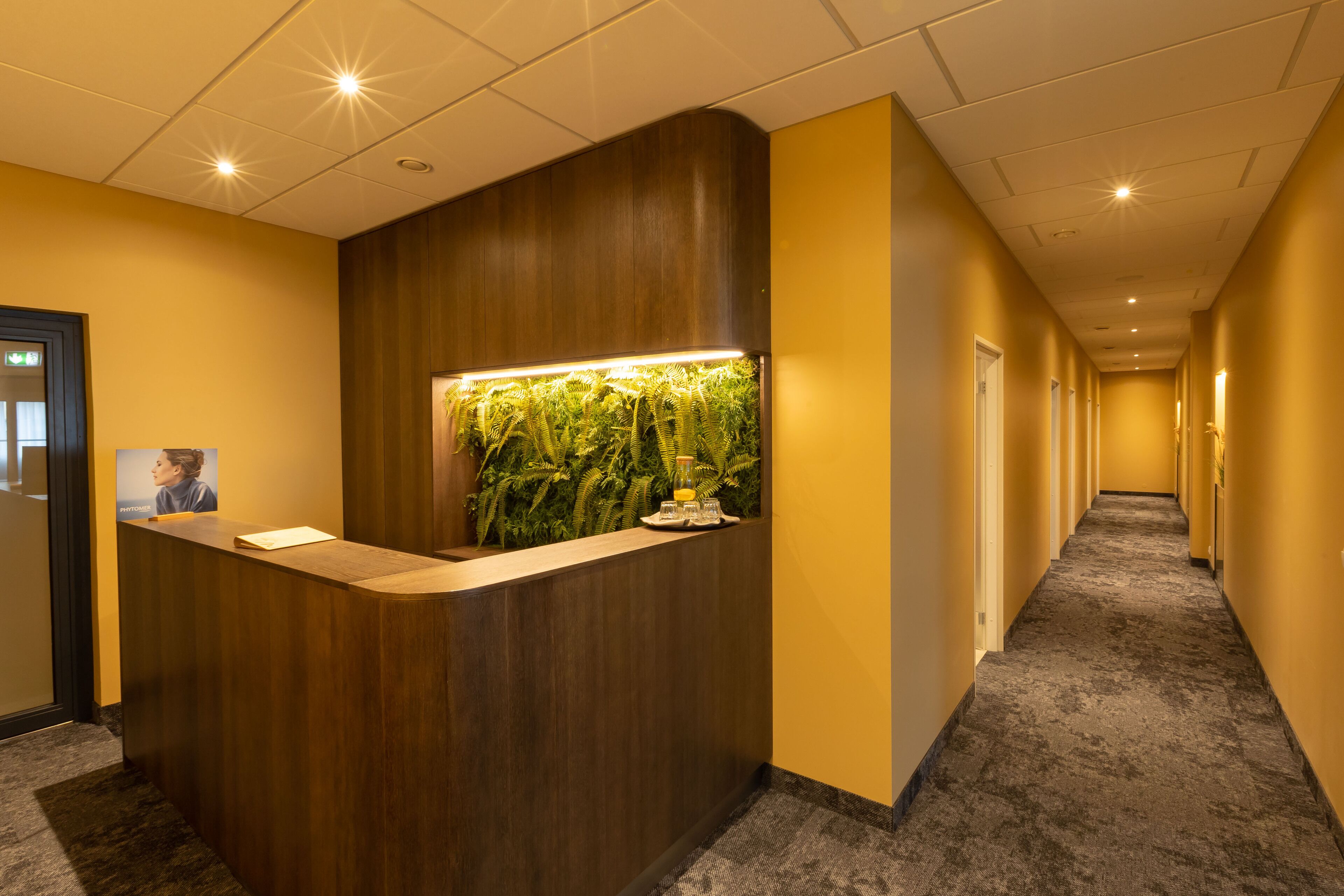 Un mostrador de recepción con detalles de madera, un jardín vertical y suelo alfombrado.