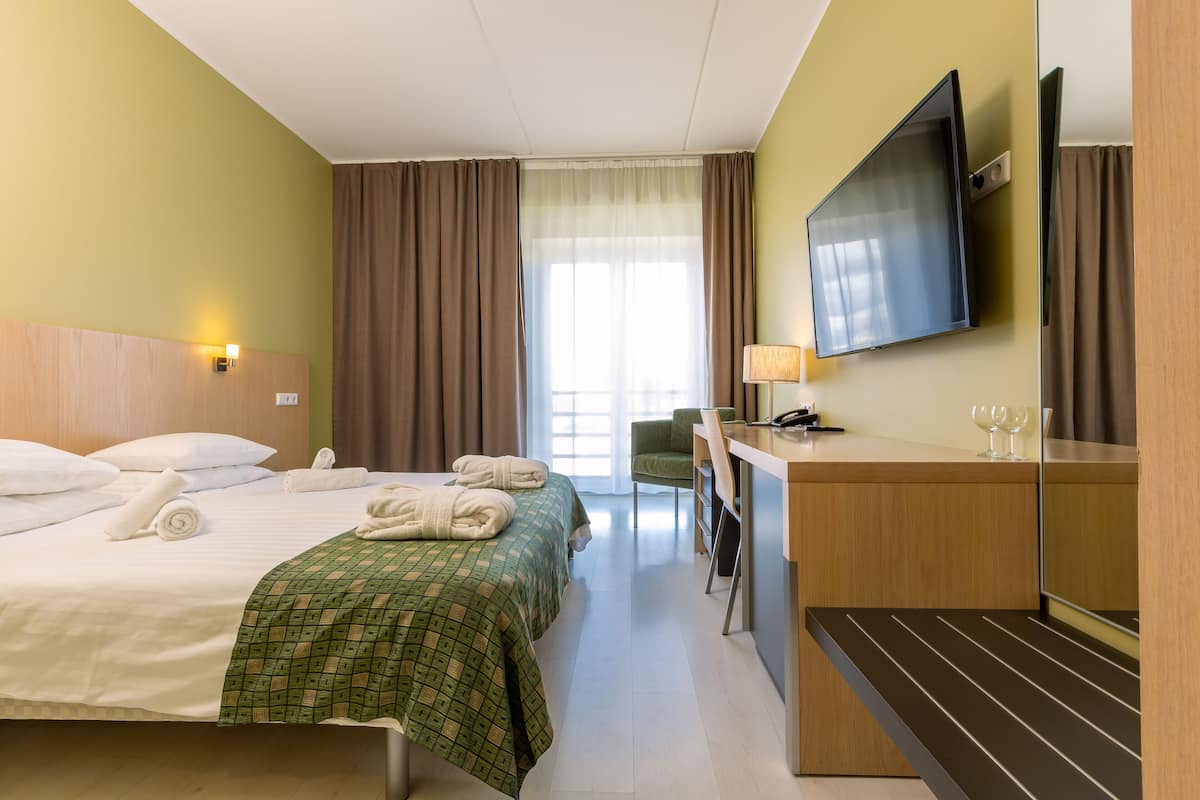 Ein Hotelzimmer mit Bett, Schreibtisch, Stuhl, Fernseher und einem fensterbepflanzten Fenster.