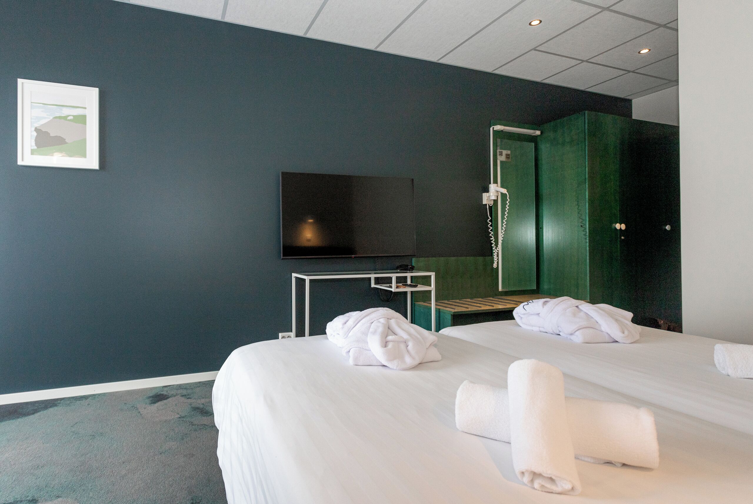 A hotel room with two beds, a television, a desk, and a green wardrobe.