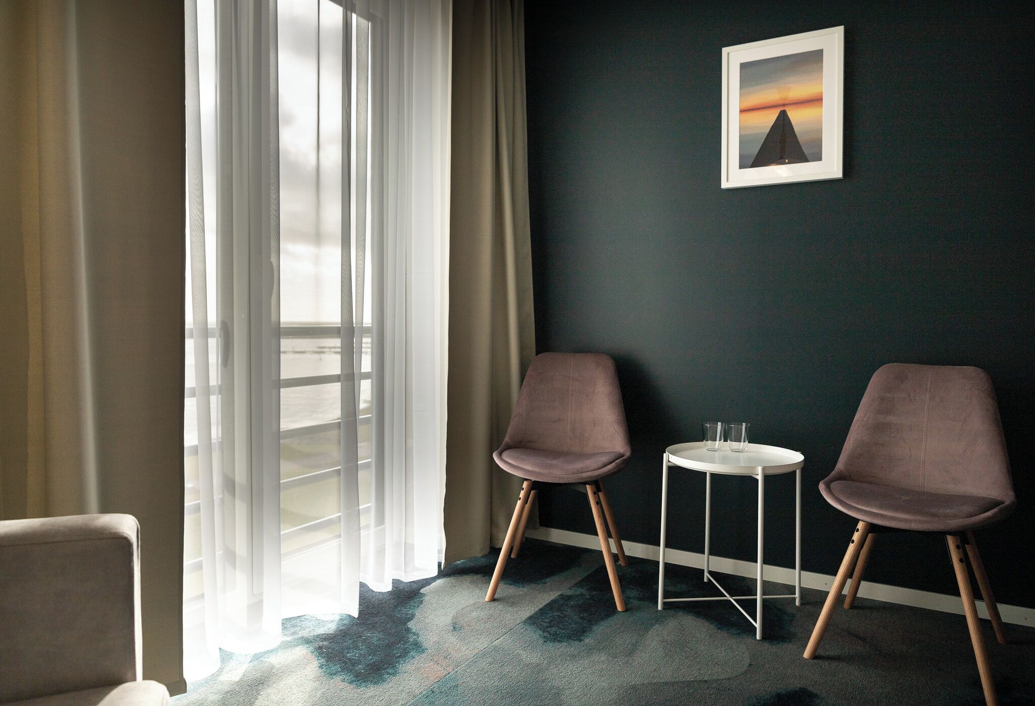 A room with two chairs, a small table, and a framed picture on the wall.