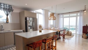A modern kitchen with a central island, bar stools, a refrigerator, and a dining area with a view. - Coastal Retreat 2BR Skyline Marina View (Río Hato)