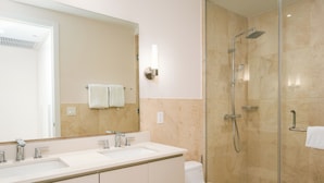 A modern bathroom with a glass-enclosed shower, a white sink with two faucets, and a toilet. - Coastal Retreat 2BR Skyline Marina View (Río Hato)