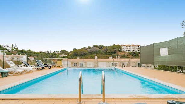 A swimming pool with lounge chairs and a view of buildings in the background. - Casa Peggy - Communal pool & garden, just 500m from the beach (Carvoeiro)