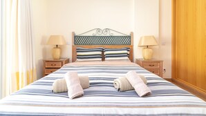 A neatly made bed with striped bedding and two pillows, two bedside lamps, and a wooden headboard. - Casa Peggy - Communal pool & garden, just 500m from the beach (Carvoeiro)