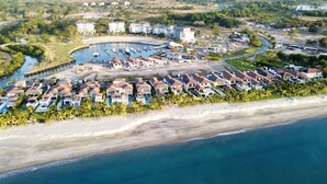 Luftaufnahme eines Küstenresorts mit mehreren bungalowsähnlichen Gebäuden, einer Marina und einem Strand.
