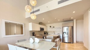 Eine moderne Küche mit weißen Schränken, einem Edelstahl-Kühlschrank und einem Essbereich mit weißem Tisch und Stühlen.