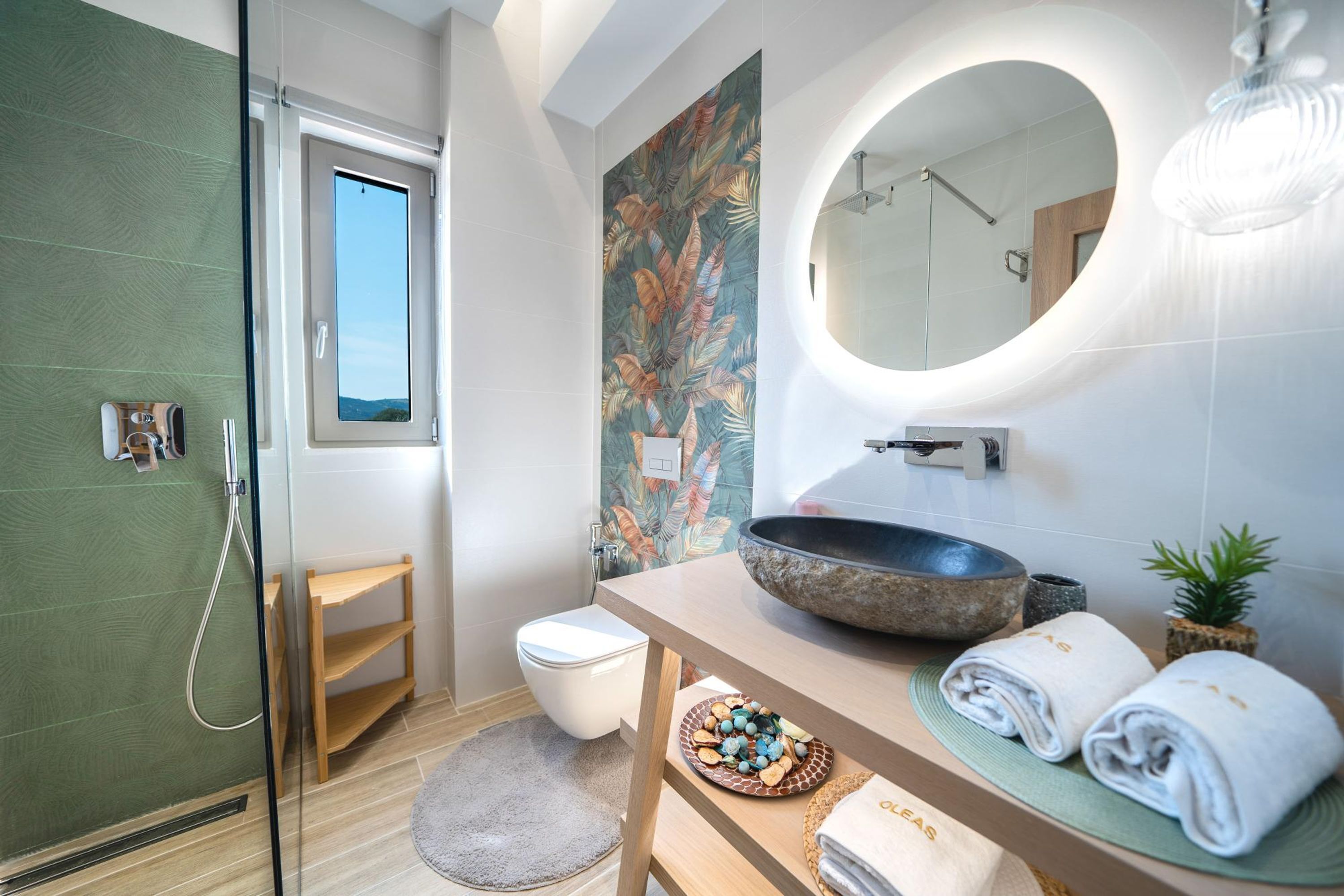 A modern bathroom with a glass shower enclosure, a toilet, a sink with a large basin, a mirror, and a small potted plant.