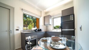 A compact kitchen with a glass dining table, built-in appliances, and a view of the outdoors. - Oleas Suite Sun Private Pool (Heraklion)