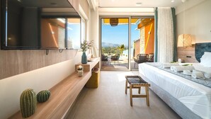 A modern hotel room with a large bed, a flat-screen TV mounted on the wall, a small seating area with a table and chairs, and a balcony with a view of the mountains. - Oleas Suite Sun Private Pool (Heraklion)