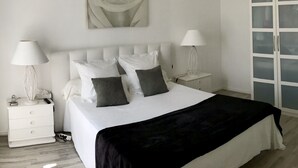 Una camera da letto con un letto, due comodini, una lampada, un quadro appeso al muro raffigurante una rosa e un armadio con ante in vetro.