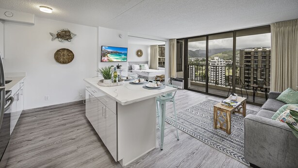 Un appartement moderne doté d’un îlot de cuisine, d’un coin repas et d’un salon avec une grande fenêtre donnant sur la ville.
